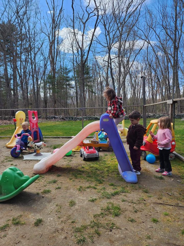 Children playing on the slide and ride-on toys in the fenced backyard