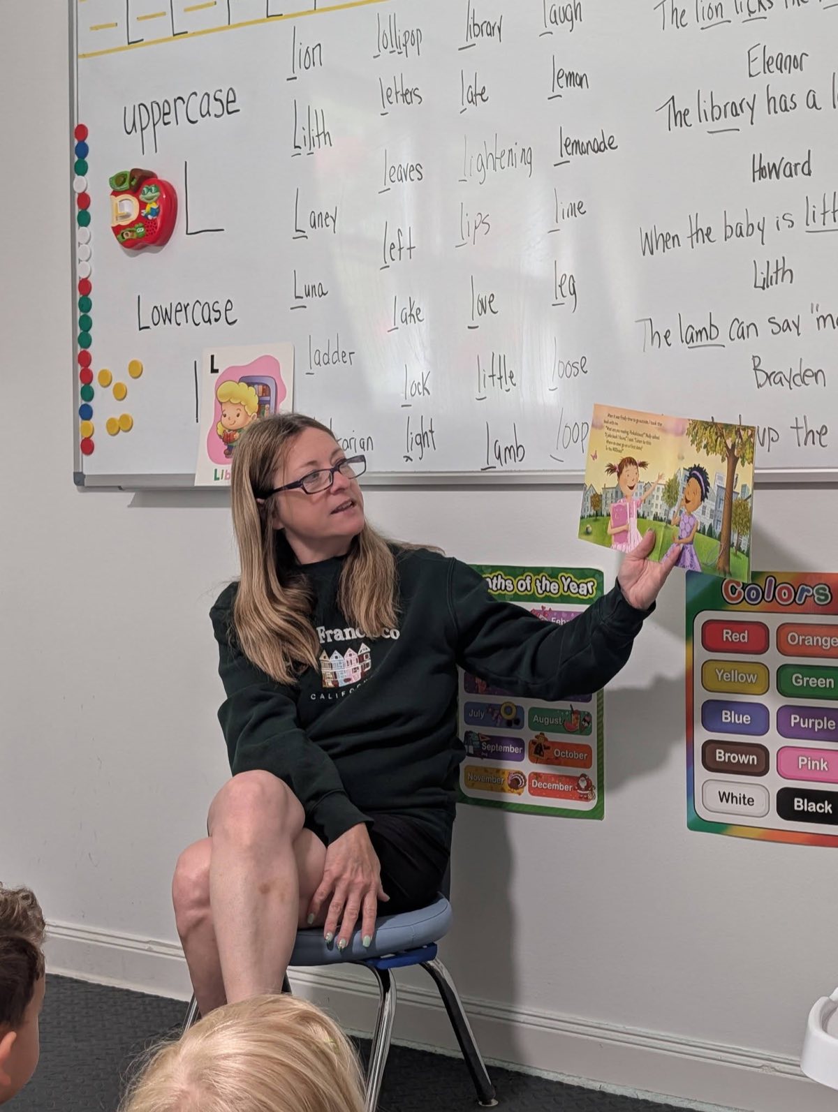 Renee holding up a picture book as she reads aloud to the children